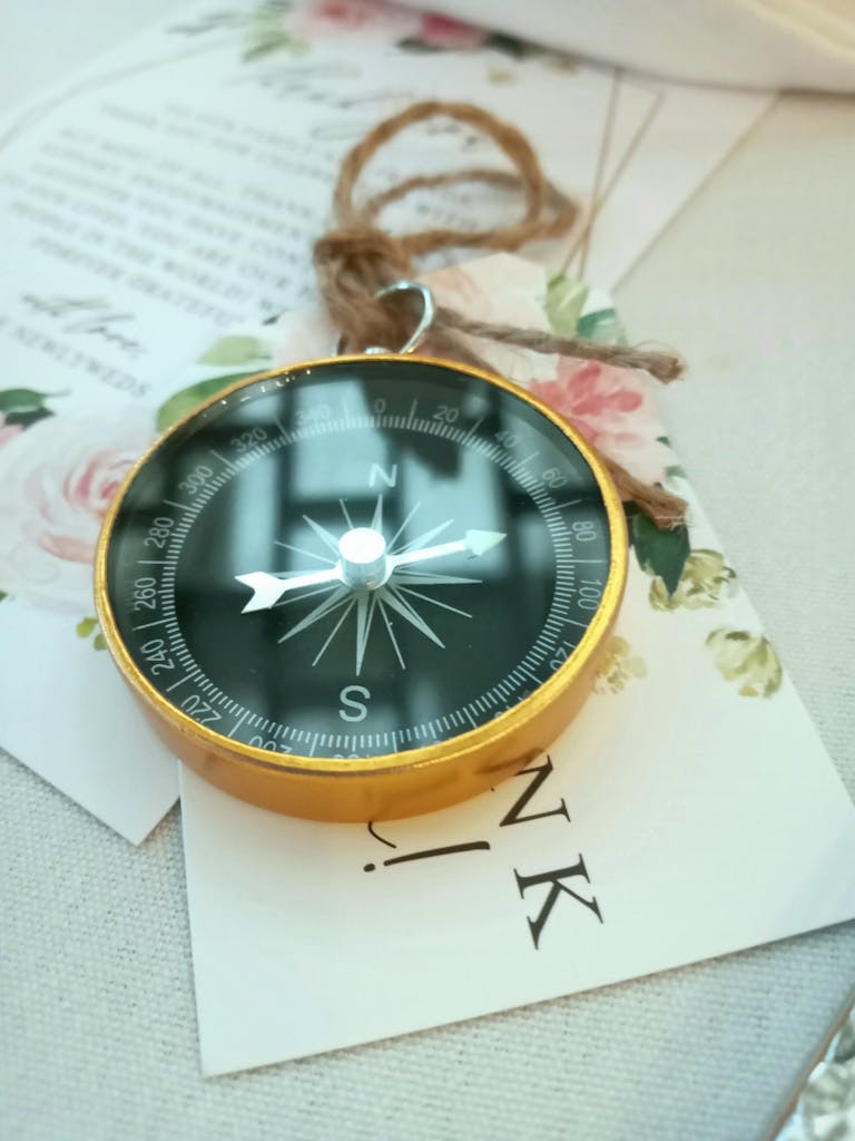 Stylish gold compass placed on a floral-themed card, suggesting elegance and exploration.